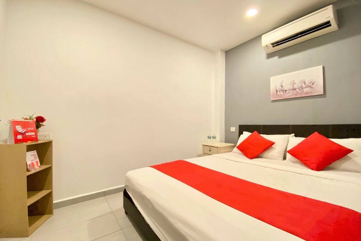 A hotel room with a bed, a nightstand, a shelf with items, and a wall-mounted air conditioner.