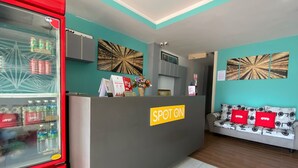 A reception area with a 'SPOT ON' sign, a refrigerator stocked with beverages, and a sofa with red cushions. - SPOT ON 90283 27 Muntri (George Town)