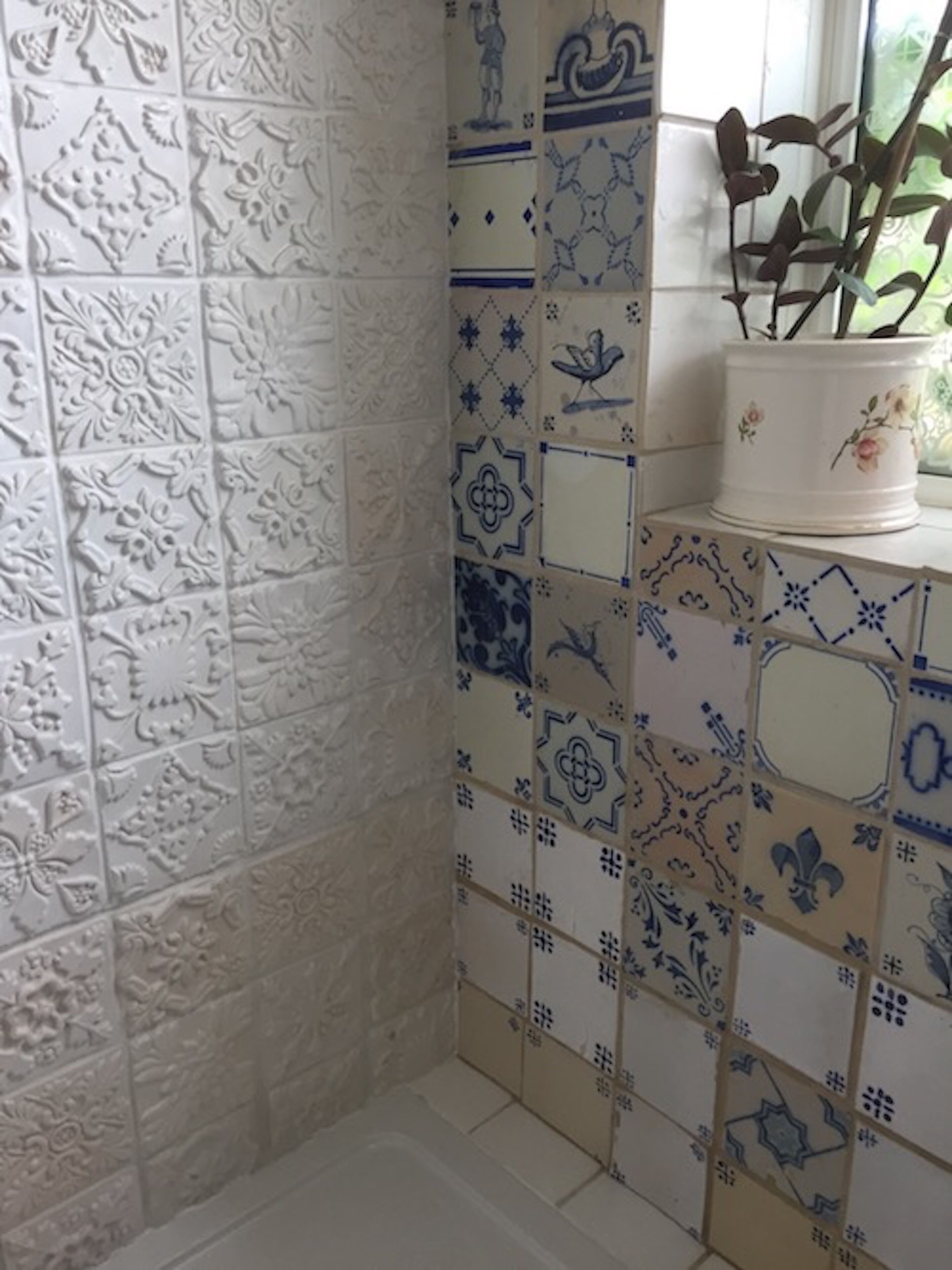 Un coin de pièce avec des carreaux décoratifs et un vase blanc orné de branches, posé sur un rebord de fenêtre.