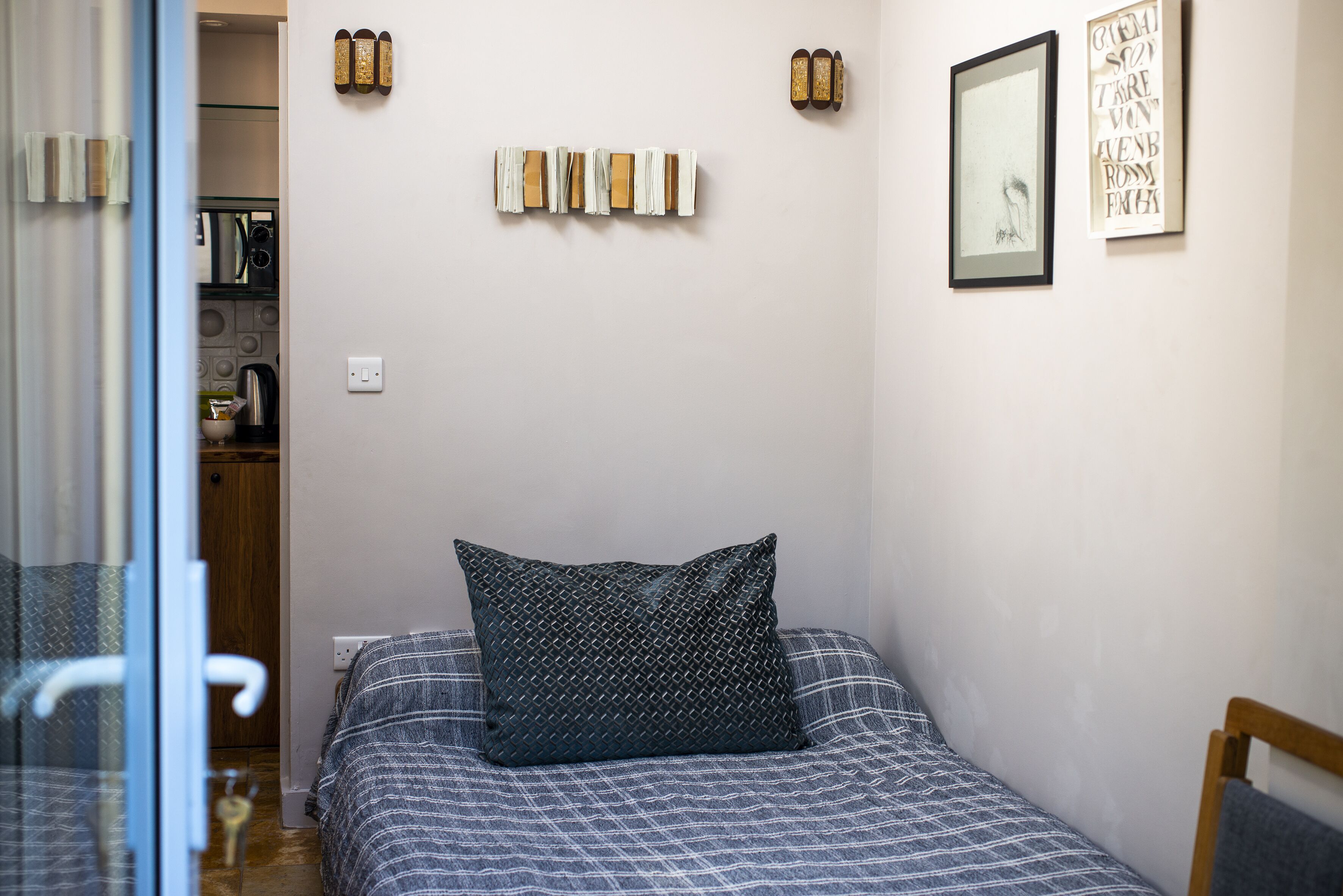 A bedroom with a bed, pillows, a framed artwork, and a wall-mounted light fixture.