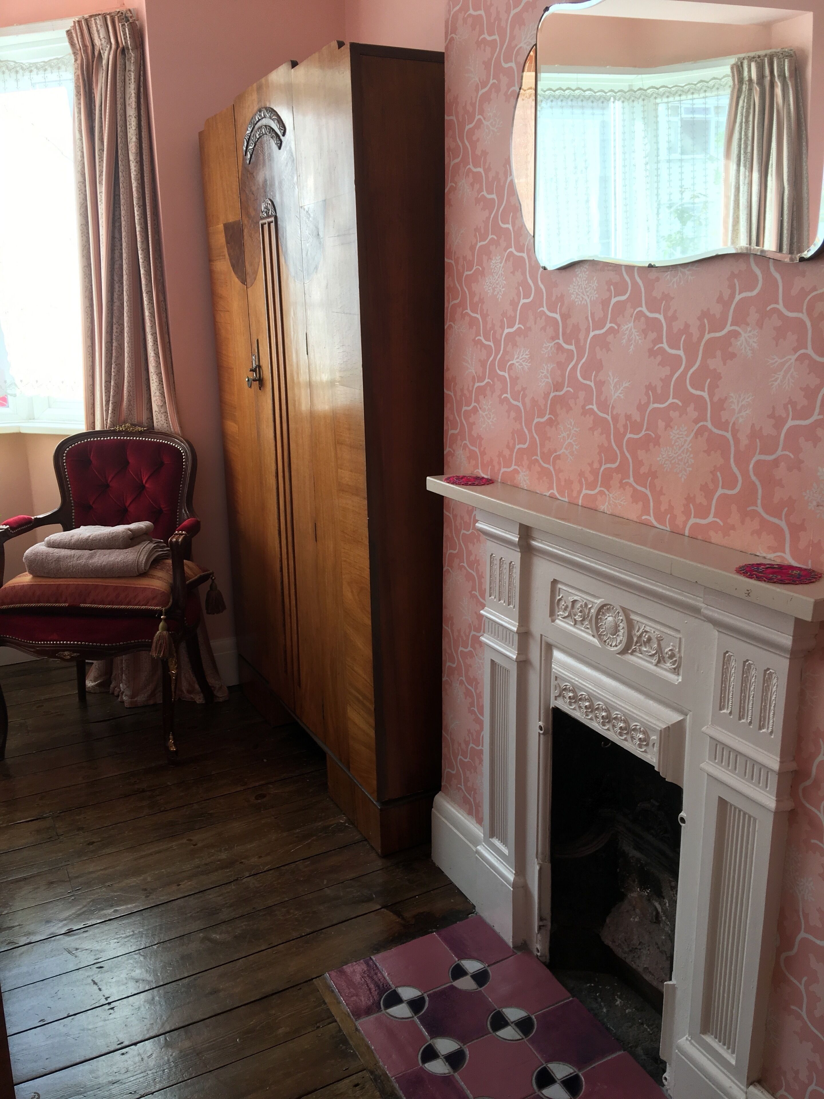 Una habitación con un armario de madera, una silla roja, una chimenea y un papel tapiz estampado.