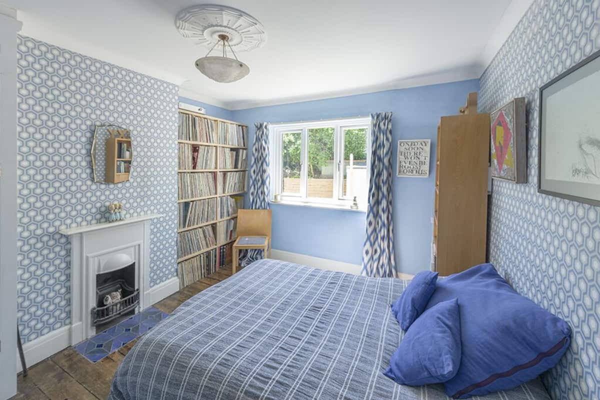 A bedroom with a large bed, a bookshelf, a fireplace, and a window with curtains.