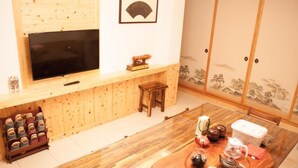 A traditional Japanese room with a TV mounted on a wooden wall, a tatami mat floor, a wooden table with tea set, and sliding doors with a landscape mural. - Yellow Mountain Homestay (Zhushan)
