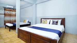 Ein Hotelzimmer mit einem großen Bett, zwei kleineren Betten, einem Deckenventilator und einer Klimaanlage.