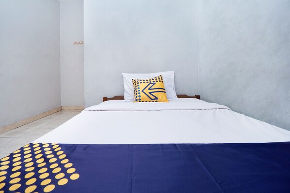 A single bed with white bedding and a blue and yellow polka dot blanket.