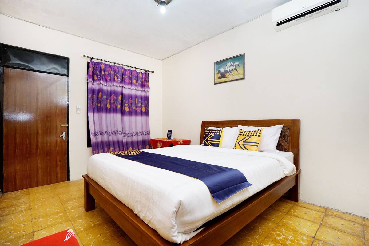 Une chambre à coucher avec un lit en bois, une table de chevet rouge, un rideau violet et un climatiseur fixé au mur.