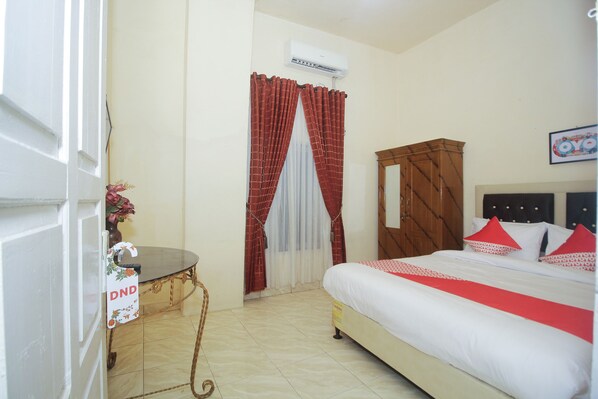 A hotel room with a bed, a wooden wardrobe, a table with a chair, and a window with curtains.