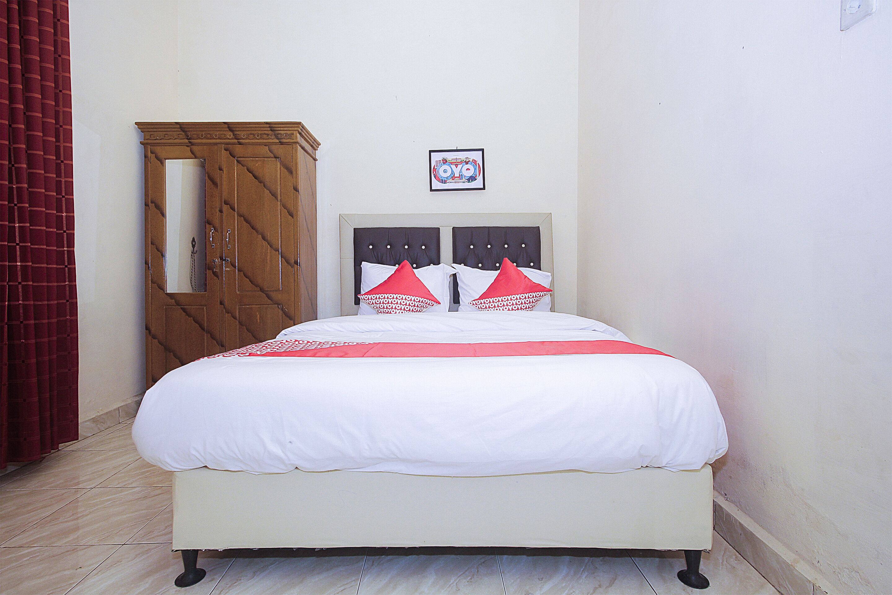 A bed with a white bedspread and red pillows, a wooden wardrobe, and a framed picture on the wall.