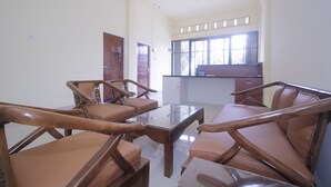 A spacious room with a high ceiling, a central glass-top table surrounded by four brown leather chairs, and a kitchen area visible through a large window. - Hotel O Diva Residen Syariah (Jambi)