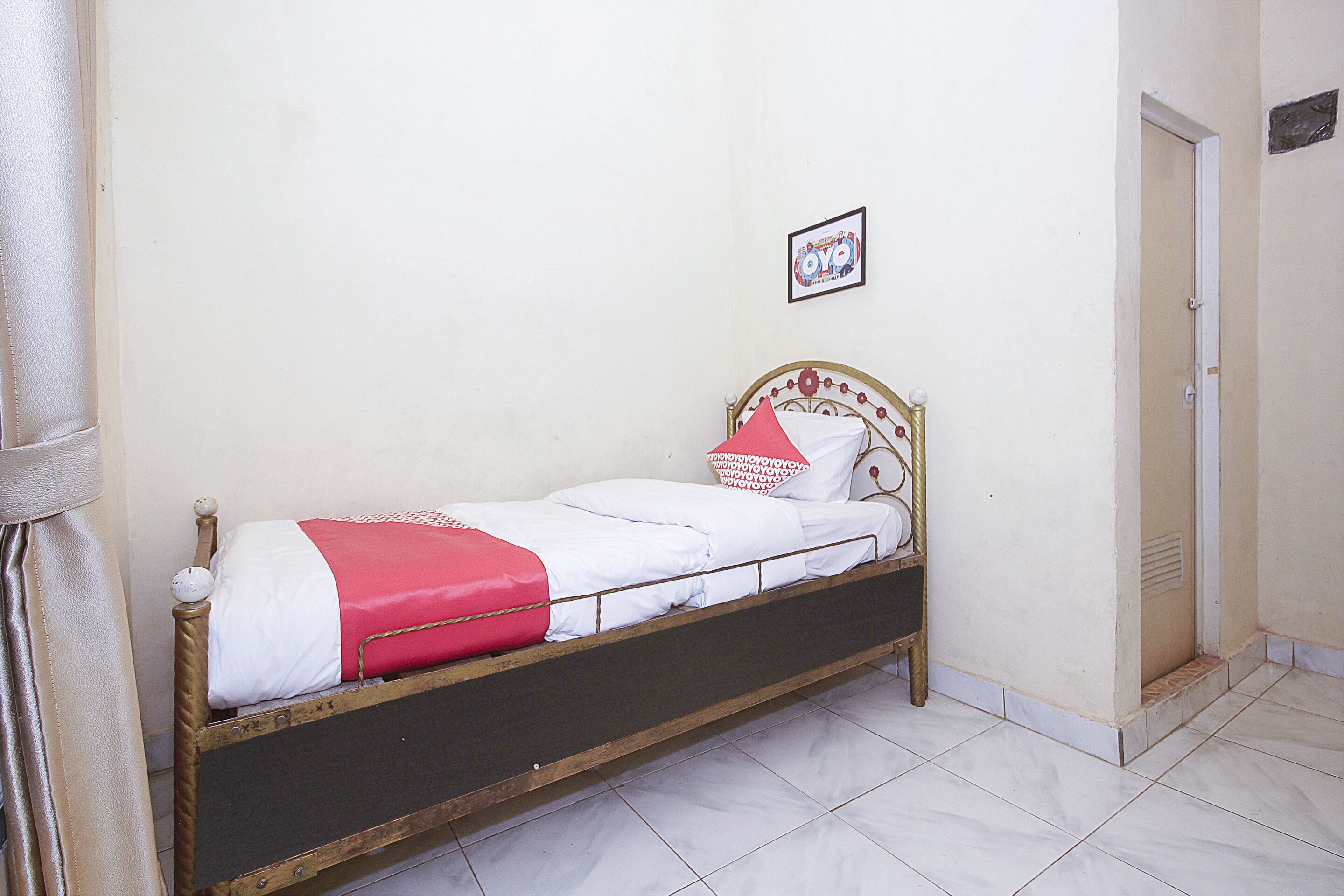 Een enkel bed met houten frame en wit beddengoed, inclusief een rode deken en kussens.