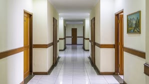 A long, narrow hallway with wooden doors and white walls. - Super OYO Collection O 25 Hotel Baltika (Bandung)