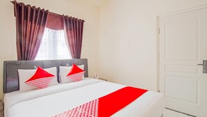 A neatly made bed with white and red bedding, a dark headboard, and red curtains.