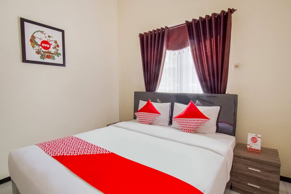 A neatly made bed with a red and white bedspread, two red pillows, and a framed picture on the wall.