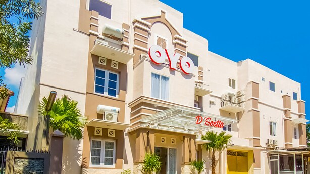 A hotel with a prominent 'OYO' sign, a covered entrance, and palm trees in front.