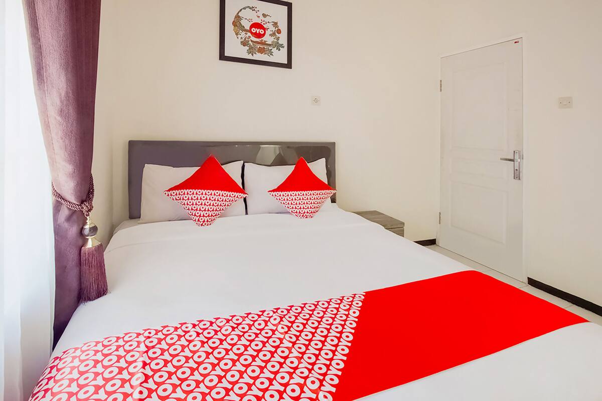 A neatly made bed with a white and red patterned bedspread, a grey headboard, and two red pillows with a circular pattern.