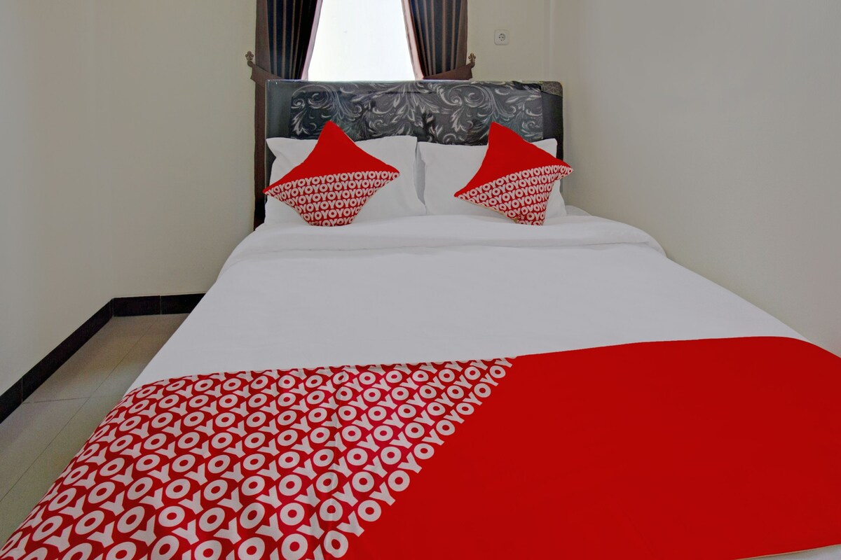 A bed with a white and red patterned bedspread, two red pillows with a repeating pattern, and a headboard with a gray and white design.