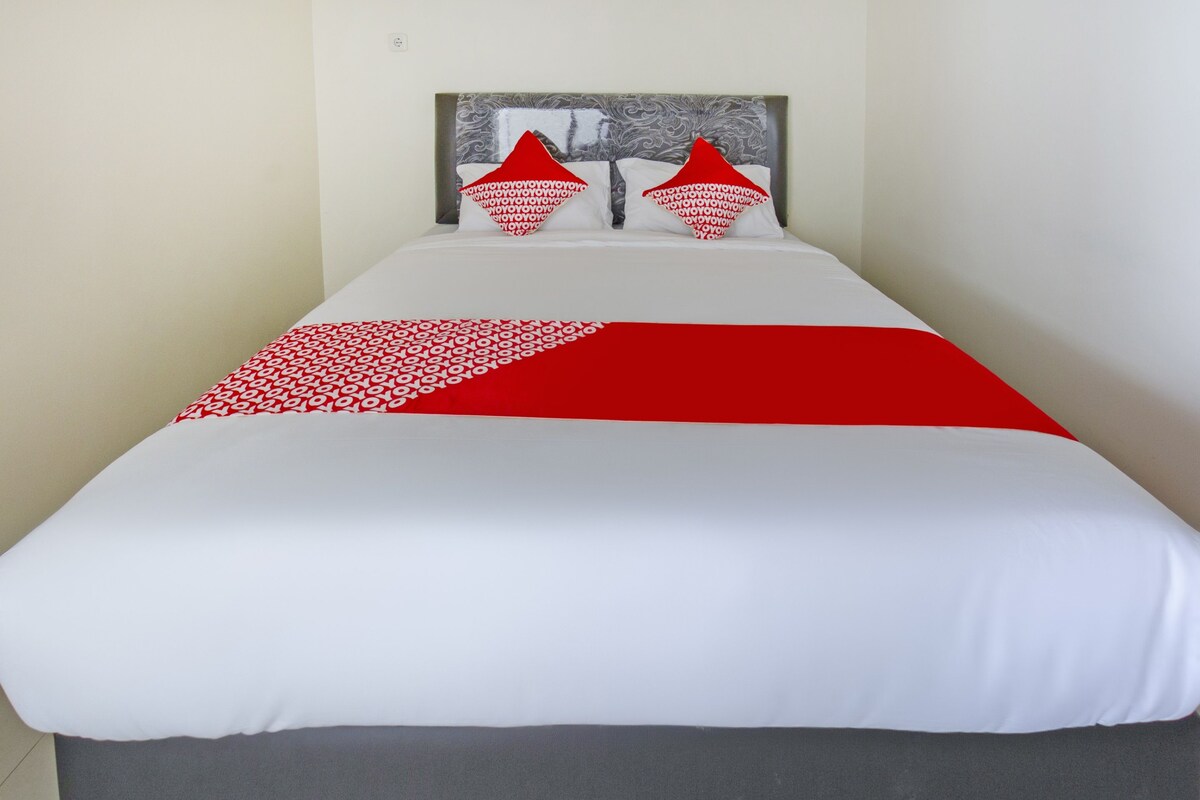 A bed with a white and red bedspread, two red pillows, and a headboard with a patterned design.