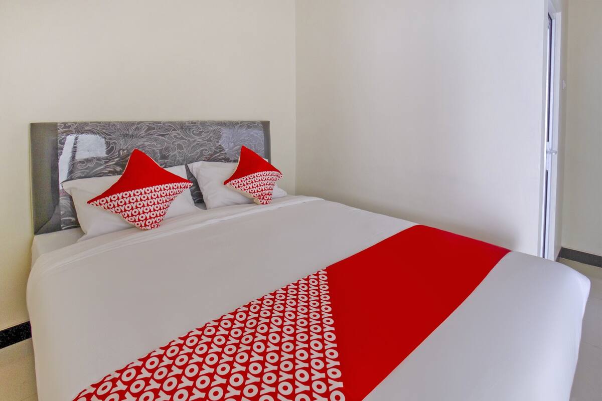A neatly made bed with a white and red bedspread, two pillows with a red and white pattern, and a grey headboard.