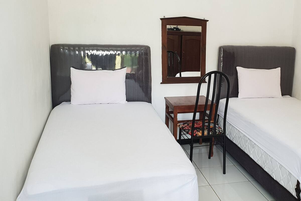 A room with two single beds, a wooden chair, a small table, and a mirror on the wall.