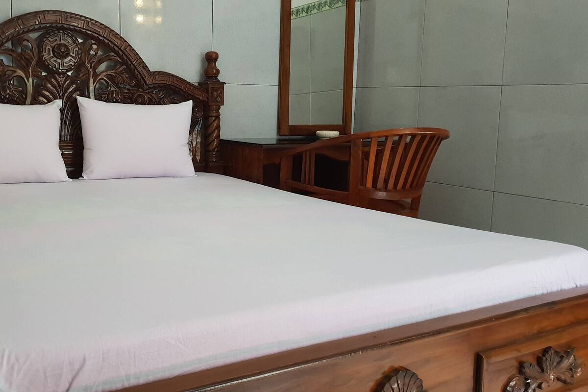 A bed with a wooden headboard, two pillows, and a wooden nightstand with a mirror.