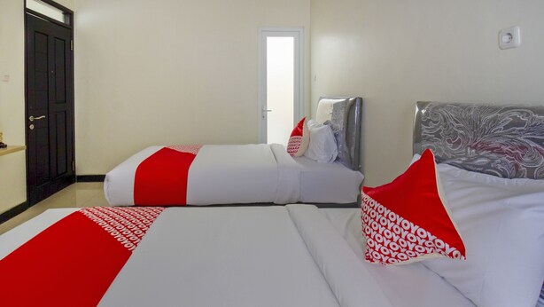 A hotel room with two beds, each with white bedding and red accents. There is a door on the left and a window on the right. - OYO 2753 Irma's Residence (Blitar)