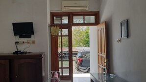A room with a wooden cabinet, a flat-screen TV mounted on the wall, and a door leading to an outdoor area with a parked car and greenery. - OYO 2753 Irma's Residence (Blitar)