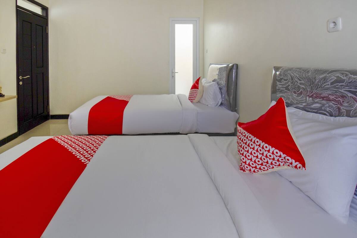A hotel room with two beds, each with white bedding and red accents.