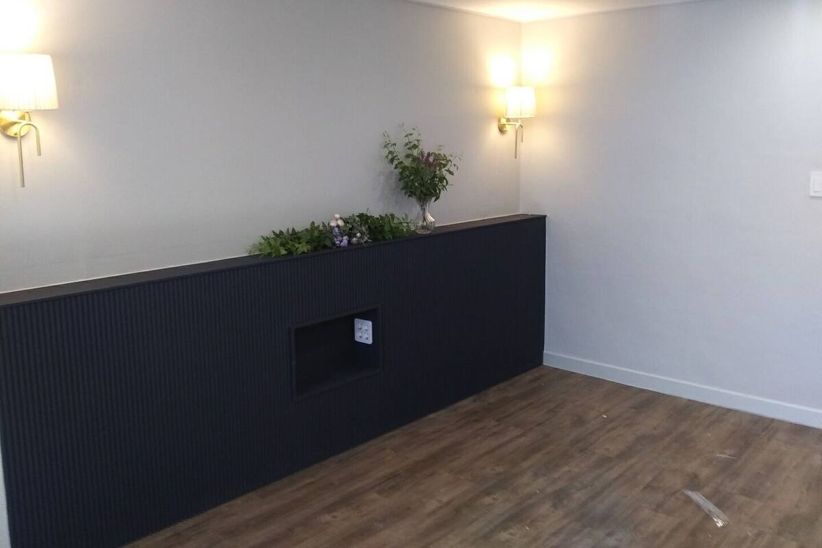 Een kamer met een donkere houten vloer, een zwart gestructureerd wandpaneel en twee wandlampen.