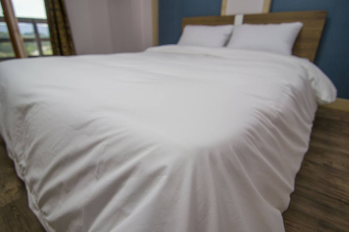 Een bed met witte lakens in een kamer met houten vloer en blauwe wanden.