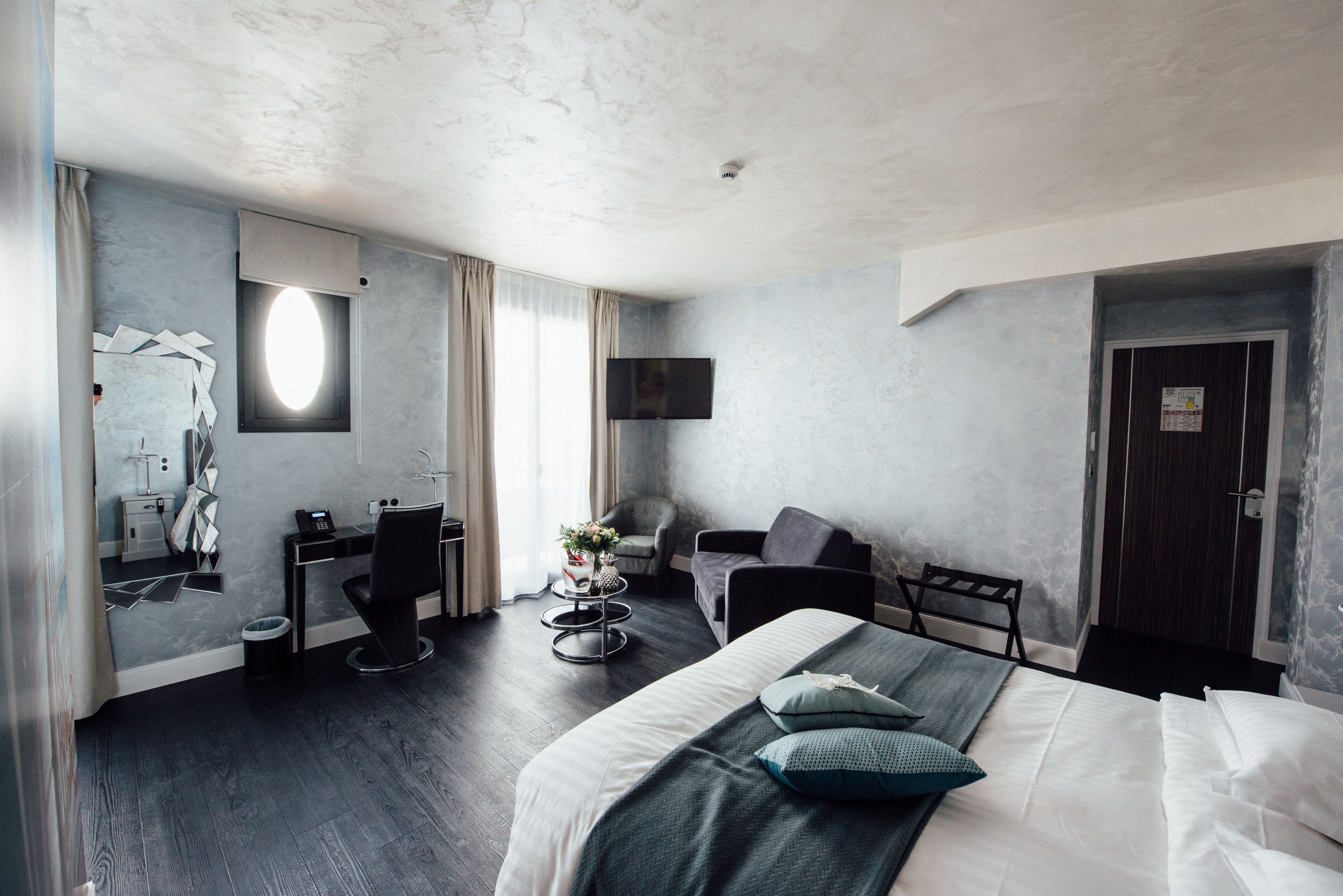 Ein modernes Hotelzimmer mit einem großen Bett, einem Schreibtisch, einem Sessel und einem Fernseher.