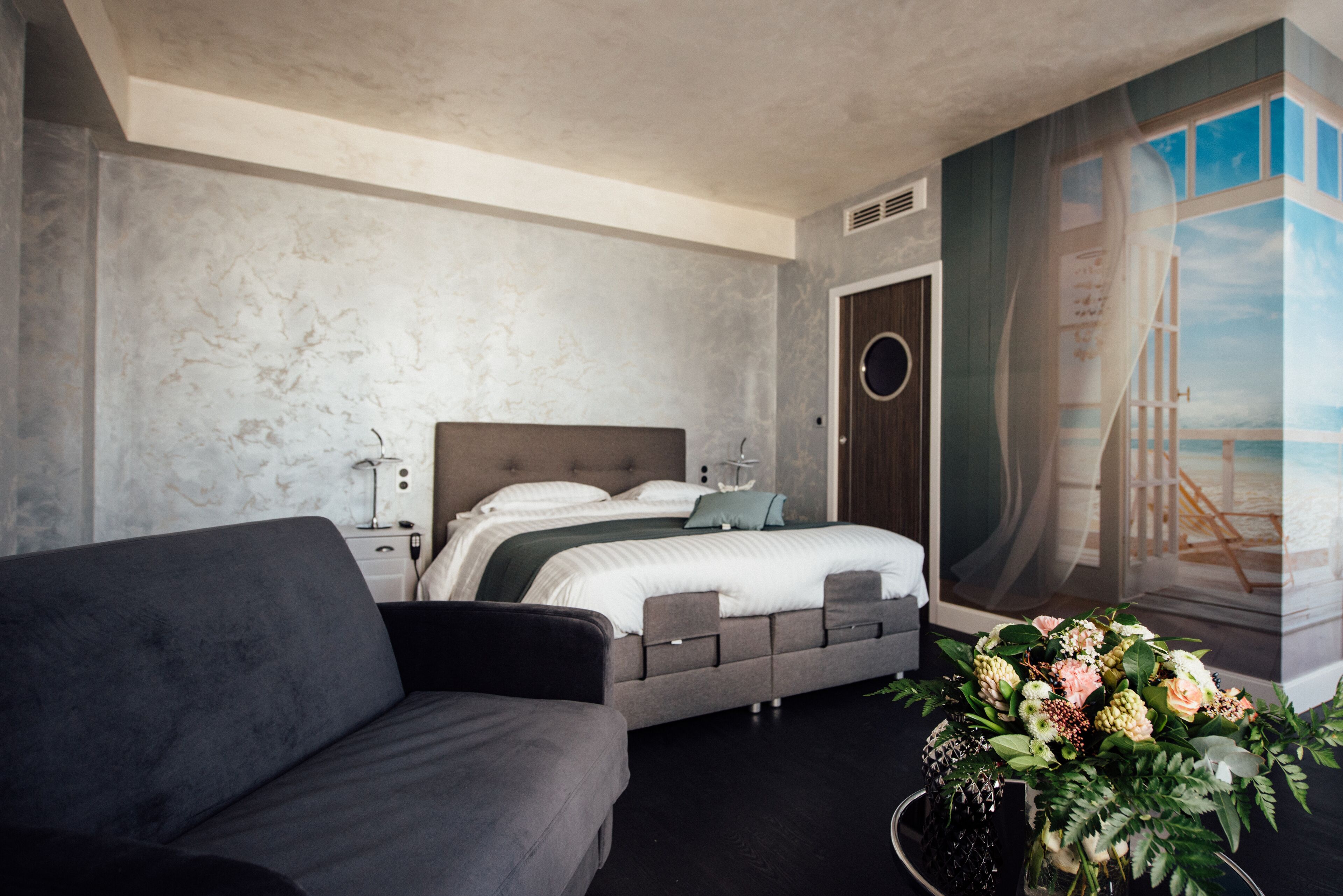 Ein modernes Schlafzimmer mit einem Bett, einem Sofa, einem Nachttisch und einem großen Fenster mit Blick.