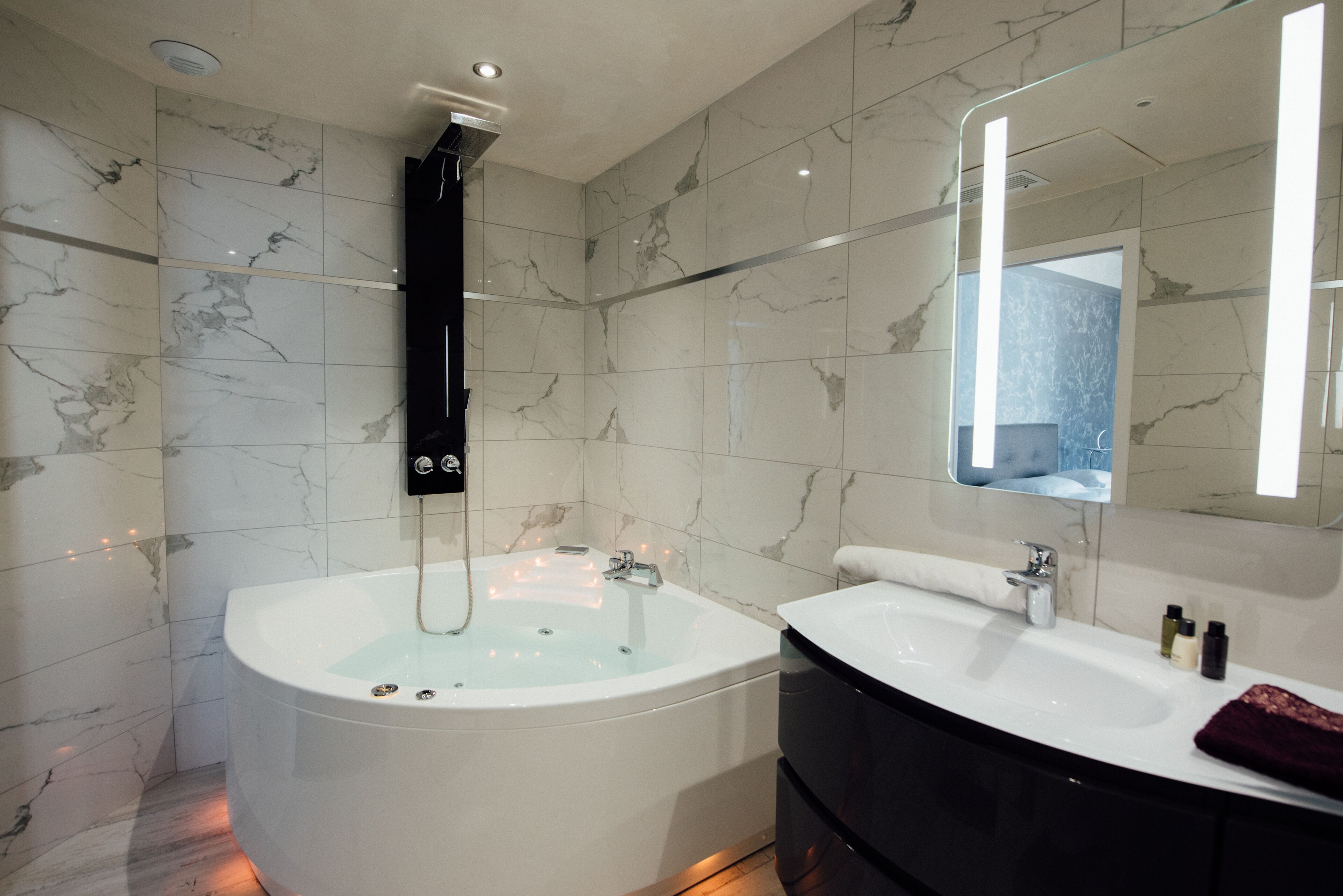 A modern bathroom with a freestanding bathtub, a vanity with a mirror, and marble walls.
