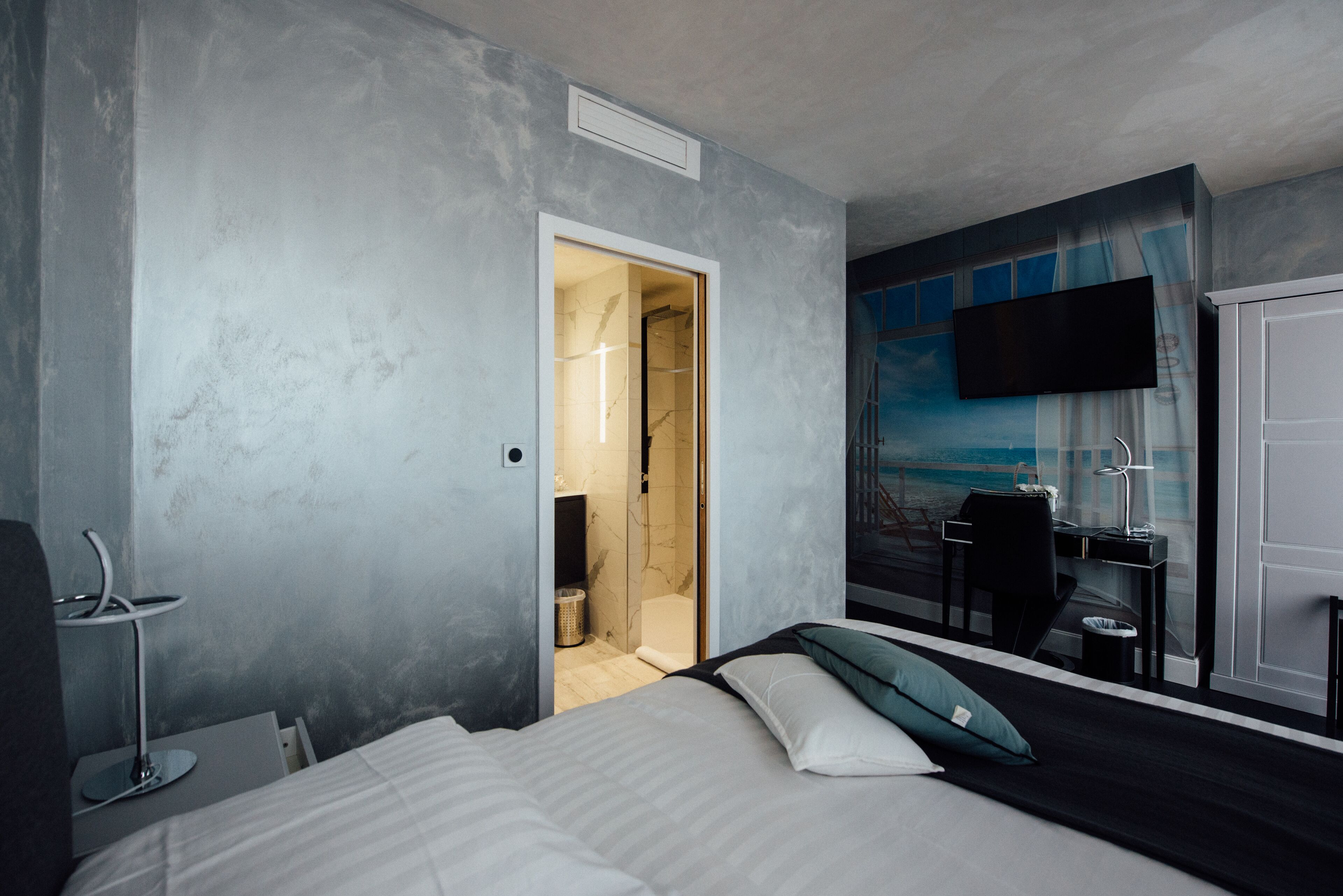 A modern hotel room with a bed, a desk, a chair, and a TV mounted on the wall.