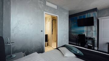 A modern hotel room with a bed, a desk, a chair, and a TV mounted on the wall.