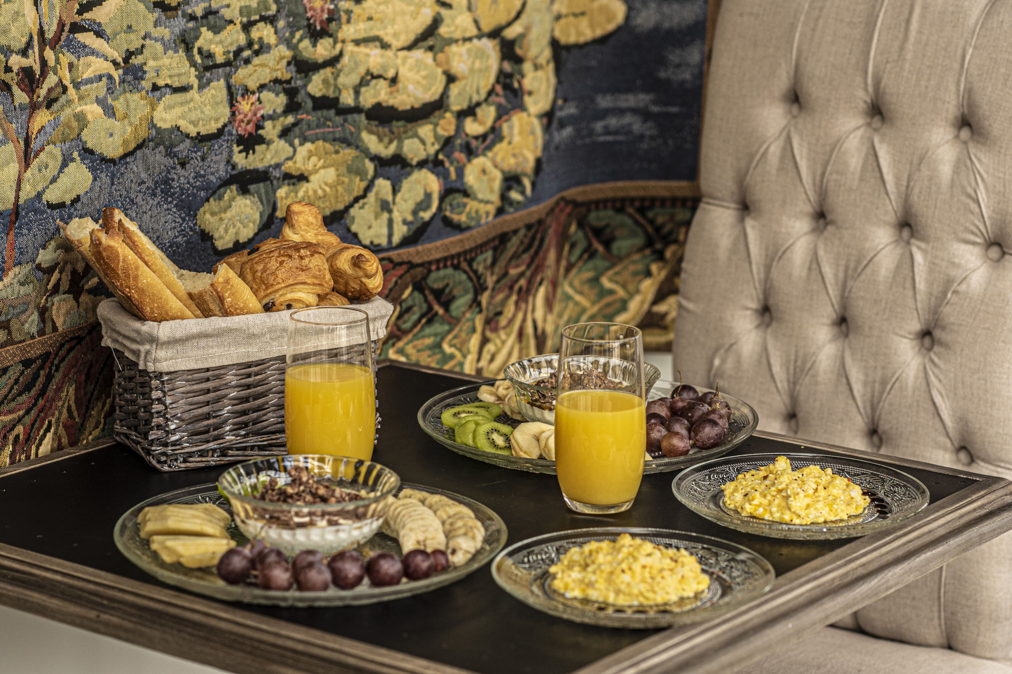Een ontbijfwagen met croissants, fruit en ontbijtgranen op een tafel met een rieten mand en een glas sinaasappelsap.