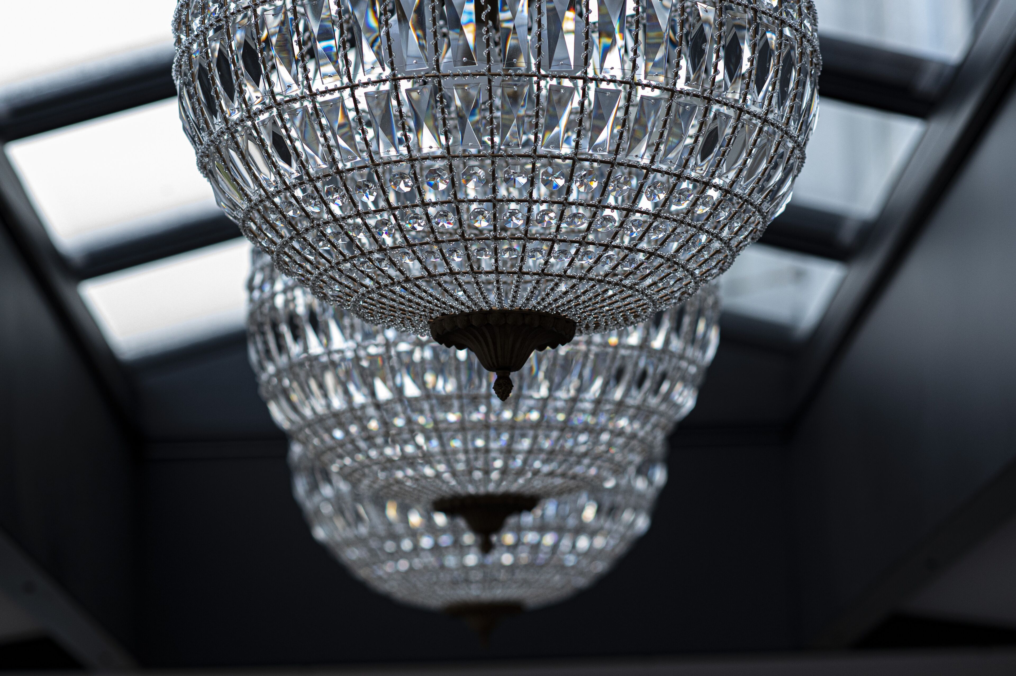 A chandelier with a geometric design, hanging from a ceiling with a skylight.