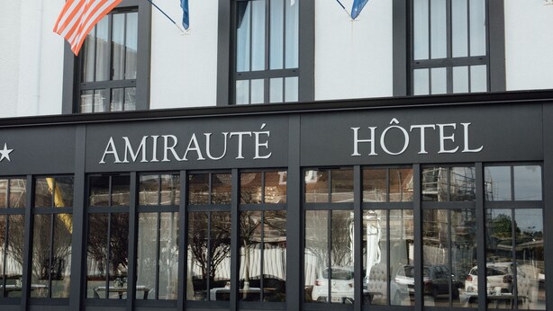 Een hotelgevel met de naam "AMIRAUTÉ HOTEL" en vlaggen van de VS, Frankrijk en de EU.
