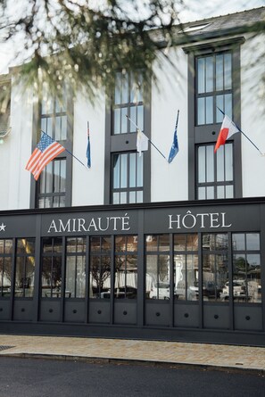 La façade d’un hôtel portant l’inscription « AMIRAUTÉ HOTEL » et arborant les drapeaux des États-Unis, de la France et de l’Union européenne.