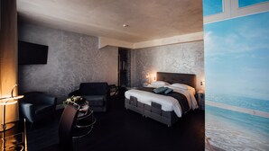 Een moderne hotelkamer met een groot bed, een bureau en een stoel. Er is uitzicht op de oceaan door een raam.