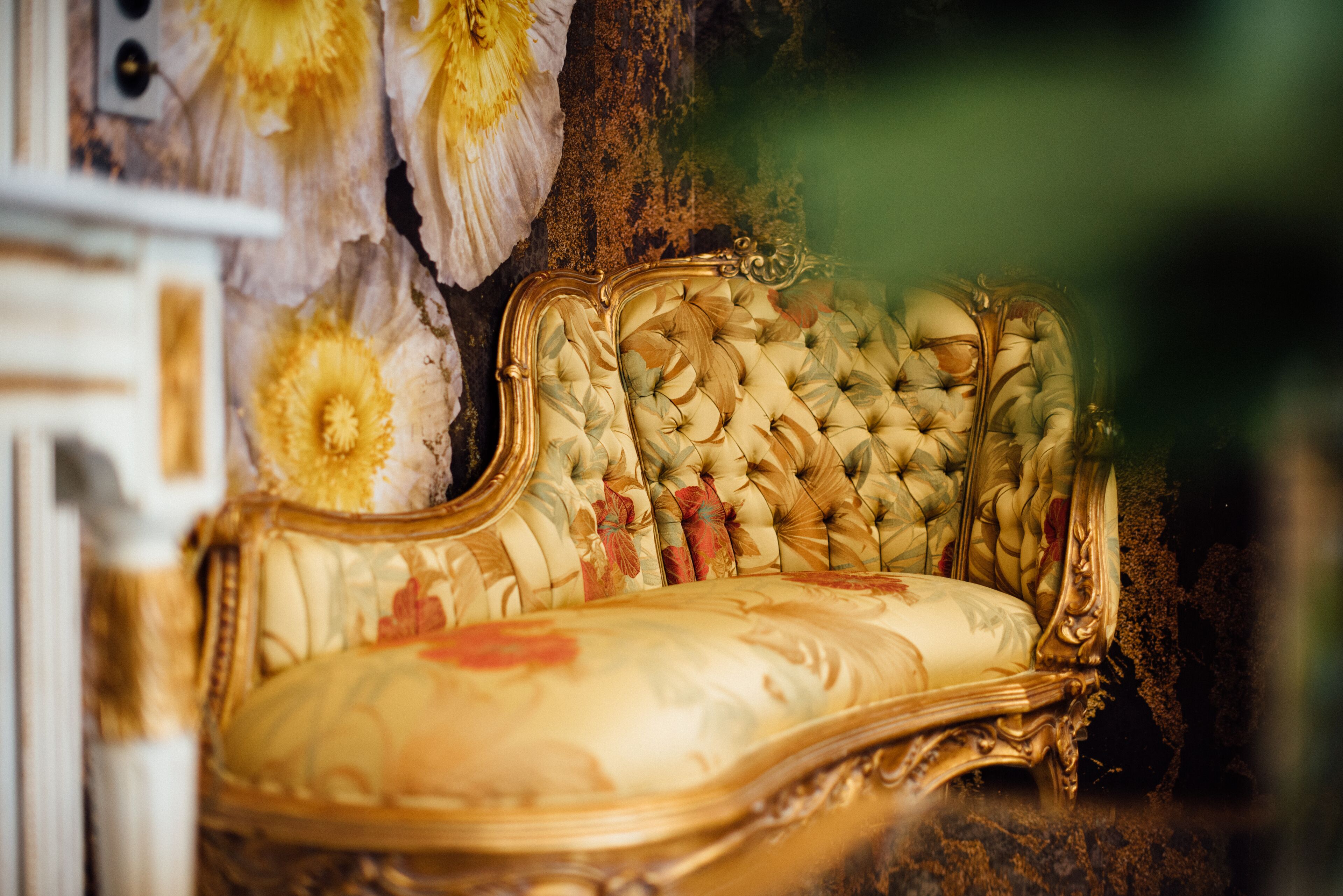 A luxurious sofa with ornate gold detailing and floral upholstery.