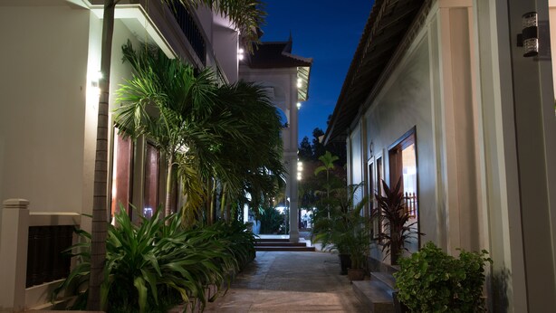 A narrow, well-lit corridor with steps leading to a central area, flanked by potted plants and buildings with illuminated windows. - ChampeySor Angkor Boutique Hotel (Siem Reap)