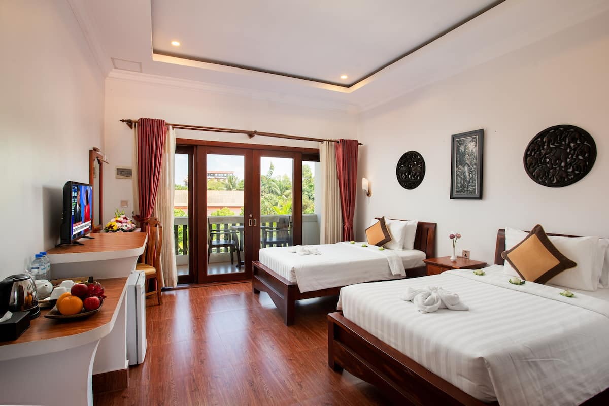 Habitación de hotel con dos camas, un escritorio con computadora y frutero, un balcón con vistas, y un televisor.