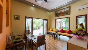 A spacious room with a wooden dining table, a sofa with yellow cushions, and a large window with curtains. - ChampeySor Angkor Boutique Hotel (Siem Reap)