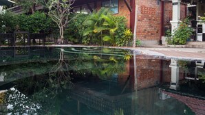 A wooden house with a balcony, surrounded by lush greenery and a reflective pool. - ChampeySor Angkor Boutique Hotel (Siem Reap)
