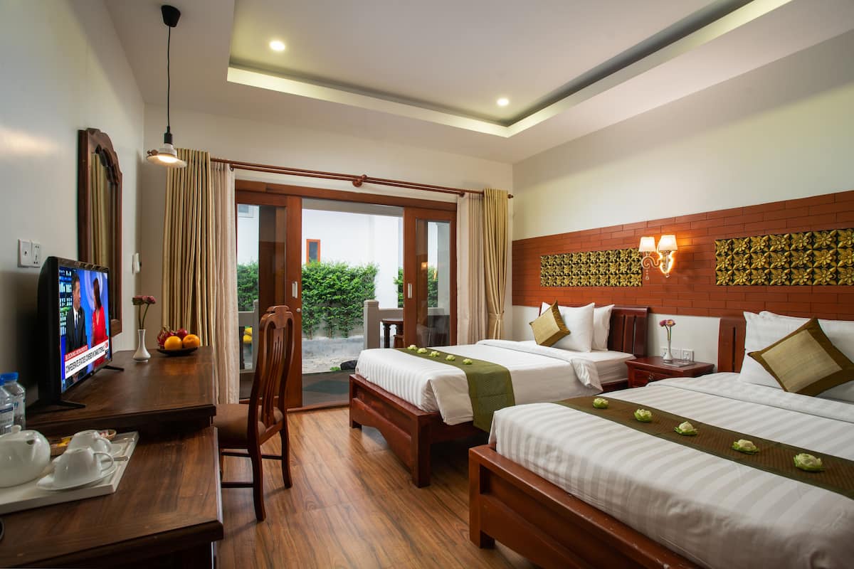 Habitación de hotel con dos camas, televisión, escritorio con silla y vista a zonas verdes.