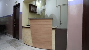 A reception area with a counter, a door, and a wall-mounted fan. - Chilika Residency (Bhubaneshwar)