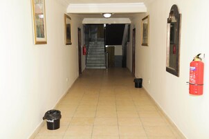 A hallway with tiled flooring, a staircase, and a fire extinguisher mounted on the wall.
