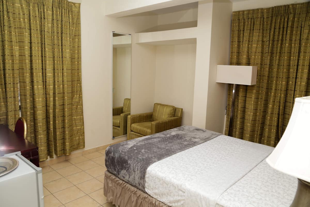 A hotel room with a bed, a chair, a lamp, and curtains.