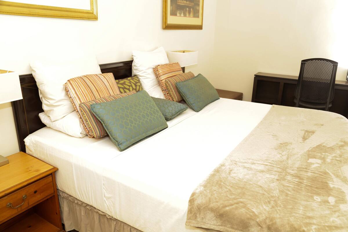 A neatly made bed with multiple pillows and a bedside table with a lamp.