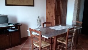 A dining area with a tiled floor, wooden chairs, a table, a cabinet, and a framed picture on the wall. - The way of "li mizzani" la jaceta (Palau)